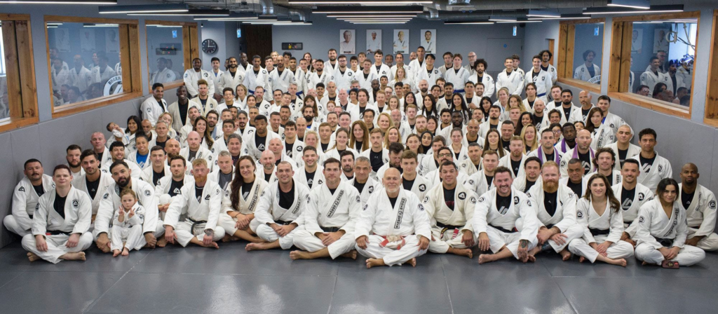 Interior da Roger Gracie Academy em Londres com atletas treinando jiu-jitsu em kimono.
