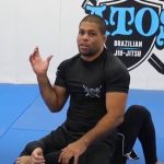 Andre Galvao ensinando tecnica com o logo da Atos Jiu-Jitsu ao fundo
