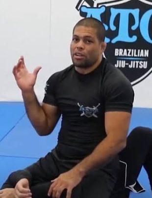 Andre Galvao ensinando tecnica com o logo da Atos Jiu-Jitsu ao fundo