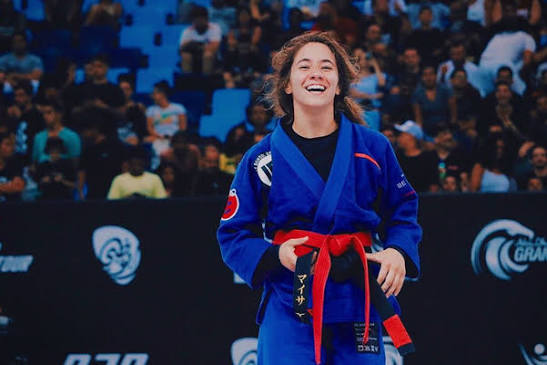 Mayssa Bastos sorrindo de kimono azul e faixa vermelha em competicao