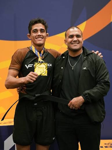 Tarcisio Damasceno Santos recebe a faixa preta ao lado do professor, com a medalha de ouro no pescoco