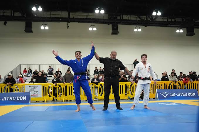 Tarcisio Damasceno Santos comemora vitoria de braco erguido de kimono azul em competicao IBJJF