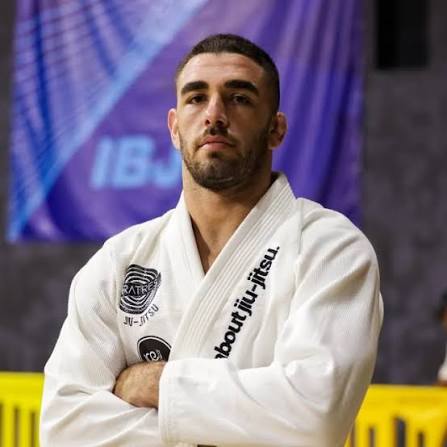 Vinicius Liberati de bracos cruzados de kimono branco em competicao de Jiu-Jitsu